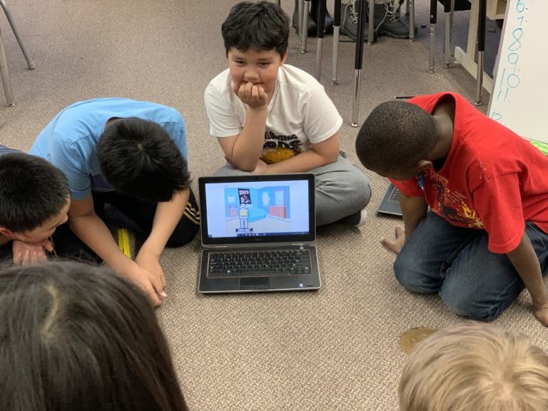 Group of young learners watching another learners scratch project.