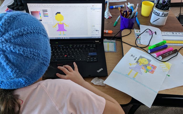 A student creating digital pixel art of a person based on a drawing.