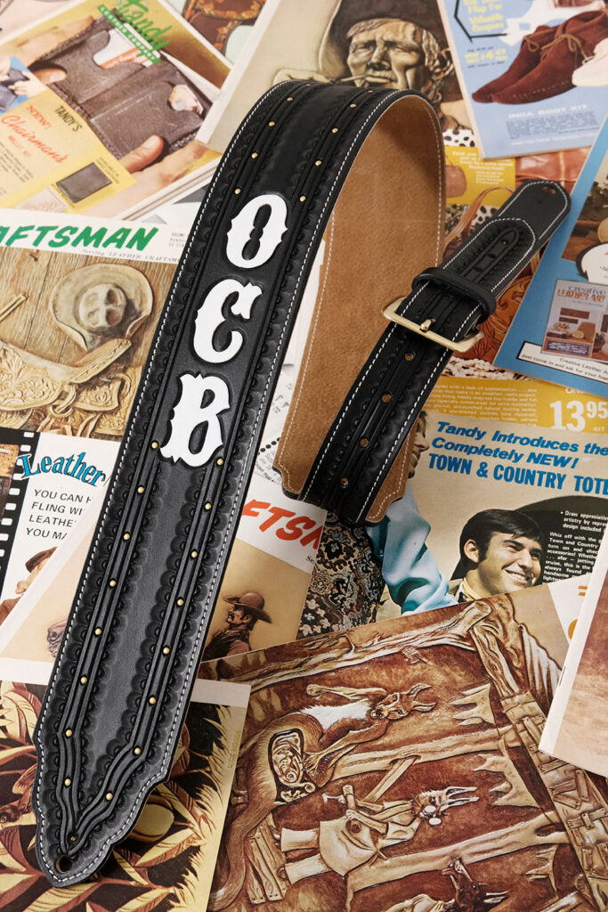 Black guitar strap with the letters O, C, B in white on it.