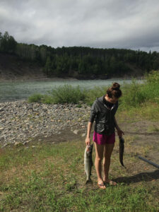 Woman standing on riverbed holding two fish.