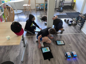 Three students use tablets to write code for the robots in the room